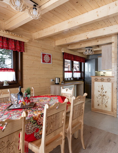 Jadalnia z widokiem na kuchnię, duży drewniany góralski stół z ozdobnymi krzesłami.