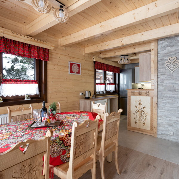 Jadalnia z widokiem na kuchnię, duży drewniany góralski stół z ozdobnymi krzesłami.