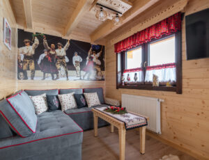 Salon w góralskim stylu z dużą kanapą, telewizorem, stolikiem i obrazem góralskiego zespołu.