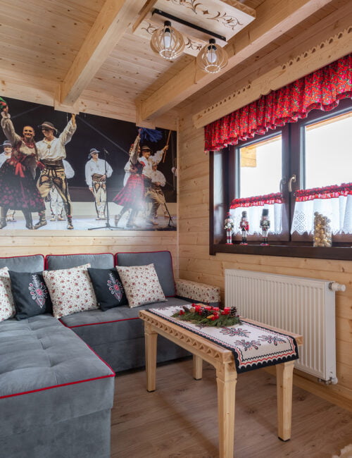 Salon w góralskim stylu z dużą kanapą, telewizorem, stolikiem i obrazem góralskiego zespołu.