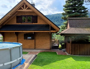 Widok na domek od strony ogrodu z basenem i szałasem do grillowania.