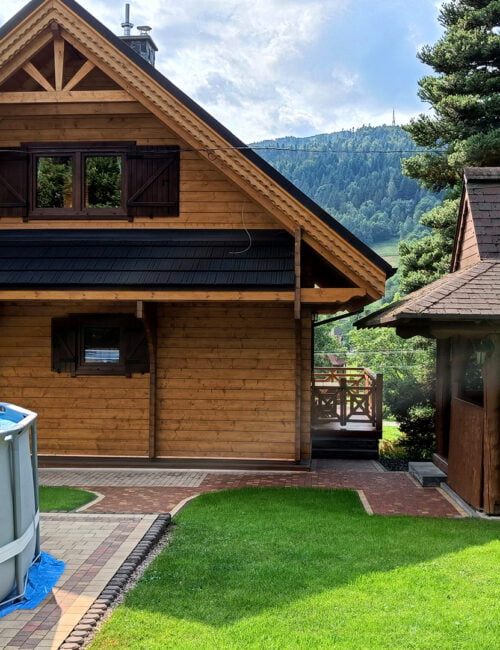 Widok na domek od strony ogrodu z basenem i szałasem do grillowania.