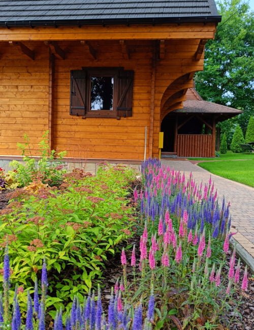 Widok na domek od boku z kolorowymi kwiatami.