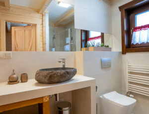 Jasna łazienka z dodatkami drewnianymi, kabiną prysznicową i kamienną umywalką.