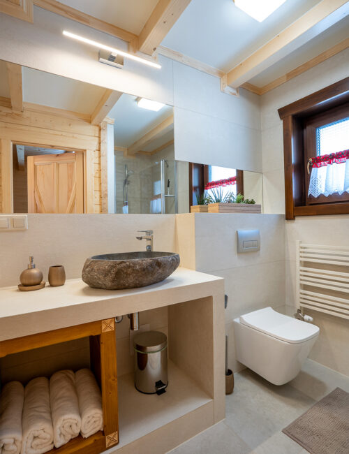 Jasna łazienka z dodatkami drewnianymi, kabiną prysznicową i kamienną umywalką.