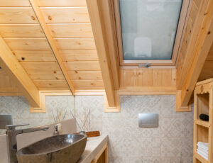 Przytulna łazienka na piętrze z oknem dachowym, w jasno szarej tonacji i drewnianymi akcentami.