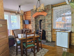 Salon utrzymany w stylu góralskim z drewnianym stołem, kanapą, telewizorem, kominkiem, parkietem, lodówka oraz boazerią na ścianach, z wyjściem na taras.