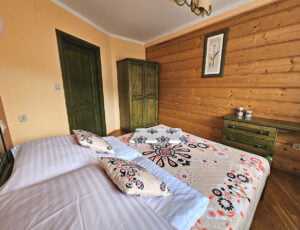 Przestronna sypialnia z łóżkiem małżeńskim, dużym oknem z widokiem na Skrzyczne, boazerią na ścianach, parkietem na podłodze, szafą oraz komodą.