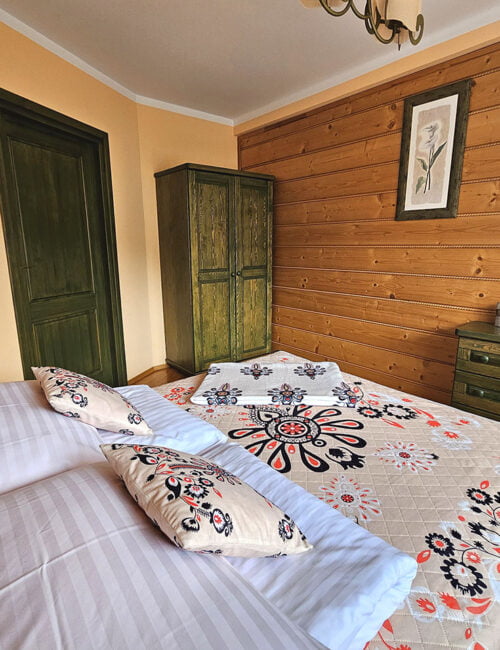 Przestronna sypialnia z łóżkiem małżeńskim, dużym oknem z widokiem na Skrzyczne, boazerią na ścianach, parkietem na podłodze, szafą oraz komodą.