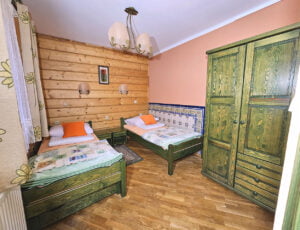 Przytulna sypialnia utrzymana w ciepłych barwach, z dwoma drewnianymi łóżkami pojedynczymi, oknem z widokiem na ogród, boazerią oraz szafą.