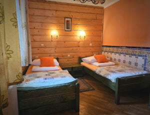 Przytulna sypialnia utrzymana w ciepłych barwach, z dwoma drewnianymi łóżkami pojedynczymi, oknem z widokiem na ogród, boazerią oraz szafą.