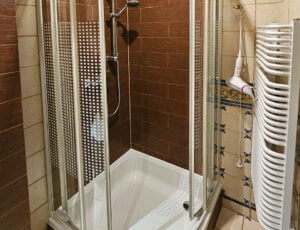 Stylowa łazienka utrzymana w jasno brązowych barwach, wyposażona w kabinę prysznicową, umywalkę, toaletę, suszarkę, grzejnik oraz ręczniki.