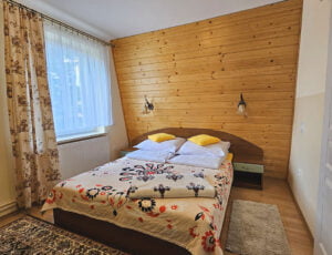 Przytulna sypialnia z łóżkiem małżeńskim, utrzymana w ciepłych barwach, z oknem, boazerią oraz wiosenną tapetą i szafą