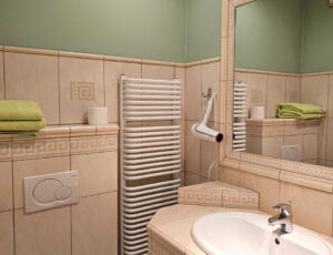 Przyjemna łazienka w kremowo-zielonych barwach, wyposażona w kabinę prysznicową, grzejnik, umywalkę, toaletę, suszarkę oraz ręczniki.