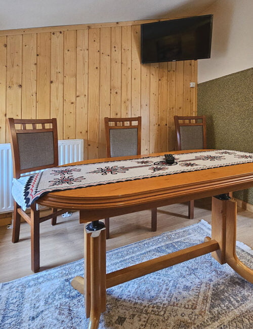 Elegancki salonik z wygodną kanapą, stołem oraz telewizorem, udekorowany boazerią, dodającą wyjątkowego uroku temu wnętrzu.