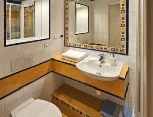 Jasna łazienka z kabina prysznicową, toaletą, umywalką, dwoma lustrami, grzejnikiem, suszarką i ręcznikami.