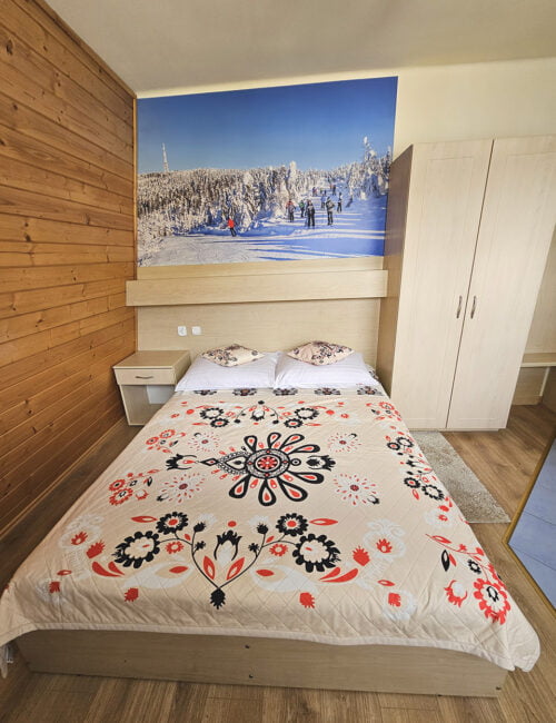 Przytulna sypialnia w kremowych tonacjach z boazerią, łóżkiem małżeńskim, szafą i obrazem zimowym ze Skrzycznego