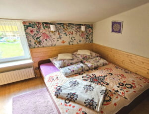 Przytulna sypialnia z łóżkiem małżeńskim i 32-calowym telewizorem, w barwach kremowych z boazerią i kwiecistą tapetą.