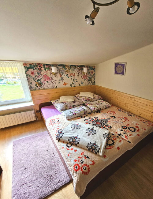 Przytulna sypialnia z łóżkiem małżeńskim i 32-calowym telewizorem, w barwach kremowych z boazerią i kwiecistą tapetą.