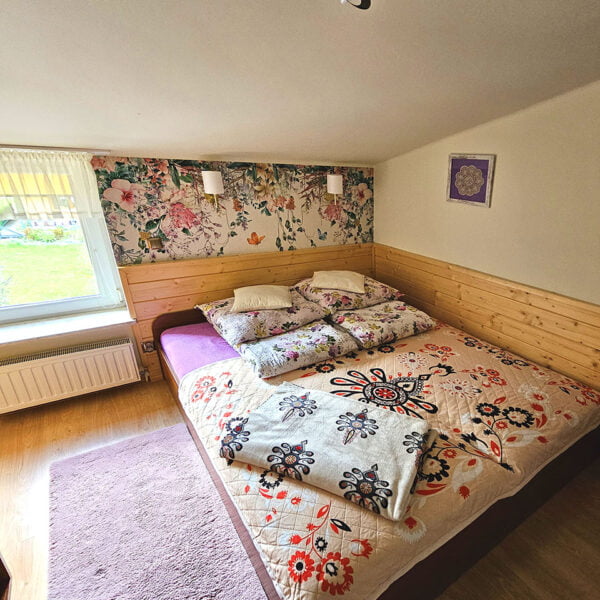 Przytulna sypialnia z łóżkiem małżeńskim i 32-calowym telewizorem, w barwach kremowych z boazerią i kwiecistą tapetą.