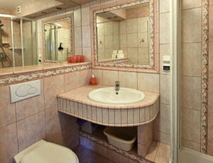 Łazienka w fioletowo-różowych barwach z toaletą, umywalką, prysznicem, suszarką i ręcznikami.