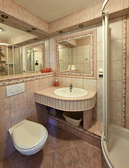 Łazienka w fioletowo-różowych barwach z toaletą, umywalką, prysznicem, suszarką i ręcznikami.