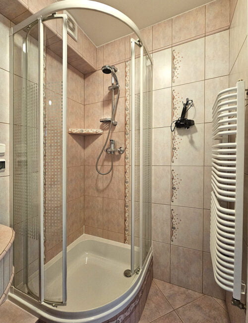 Łazienka w fioletowo-różowych barwach z toaletą, umywalką, prysznicem, suszarką i ręcznikami.