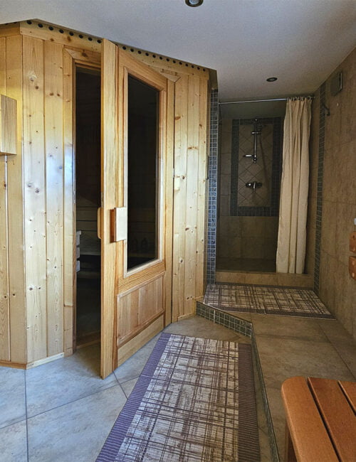Widok na całe pomieszczenie sauny w Willi Rosa, z wejściem, ławką i prysznicem, idealne dla gości szukających noclegów z wellness.