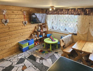 Kącik dla dzieci z zabawkami, stolikiem i TV na tle boazerii.