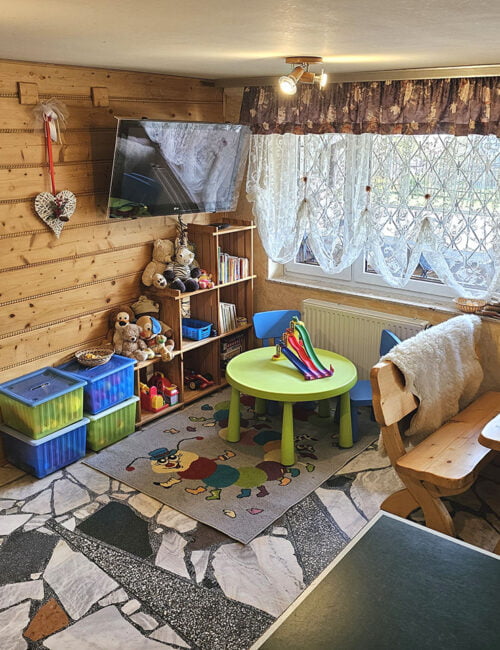 Kącik dla dzieci z zabawkami, stolikiem i TV na tle boazerii.