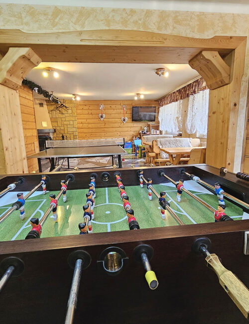 Duże, solidne piłkarzyki do gry na świetlicy, w tle drewniane ławki i stół do ping ponga.