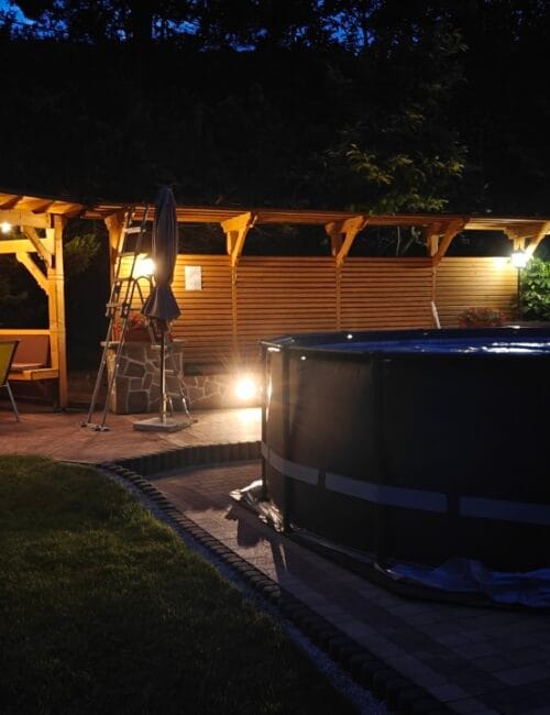 Podgrzewany basen ogrodowy nocą z oświetloną altaną w tle